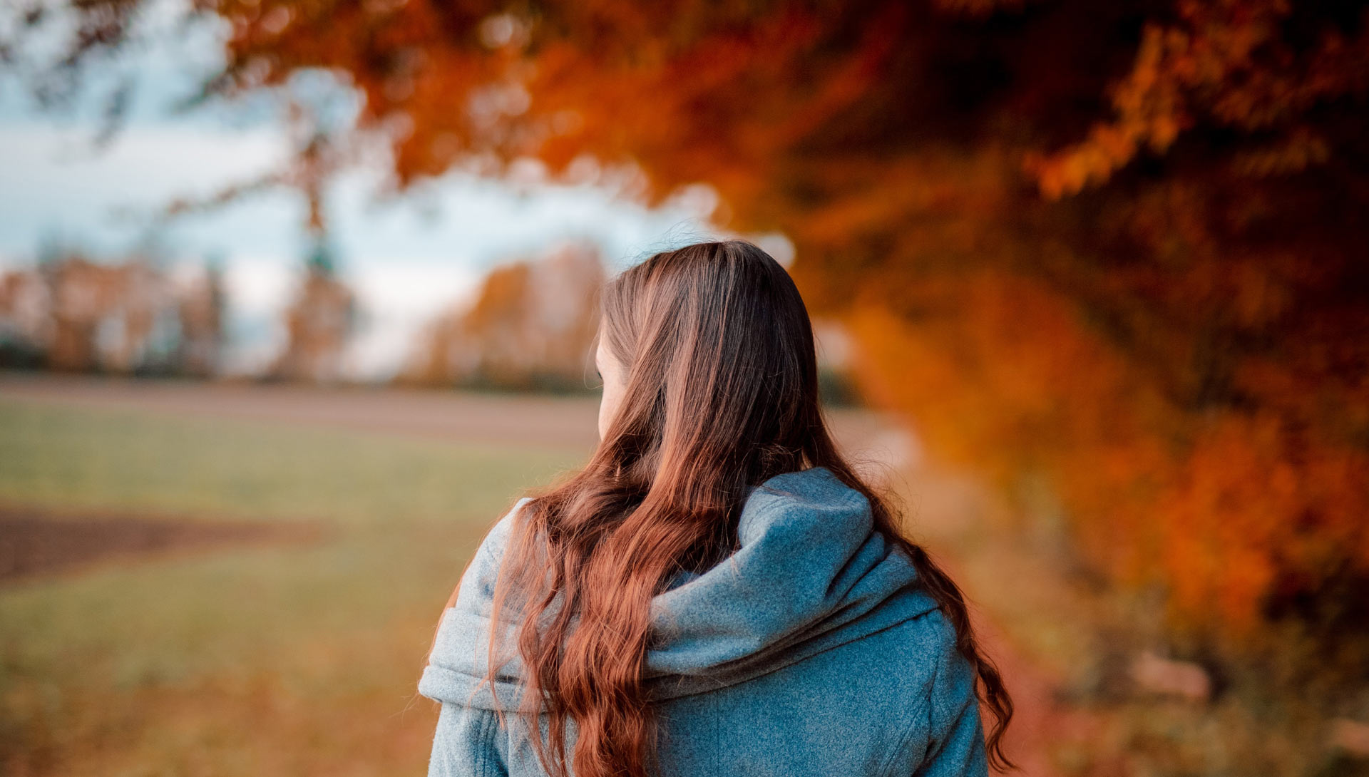 A woman walking through an autumn park among red and golden leaves